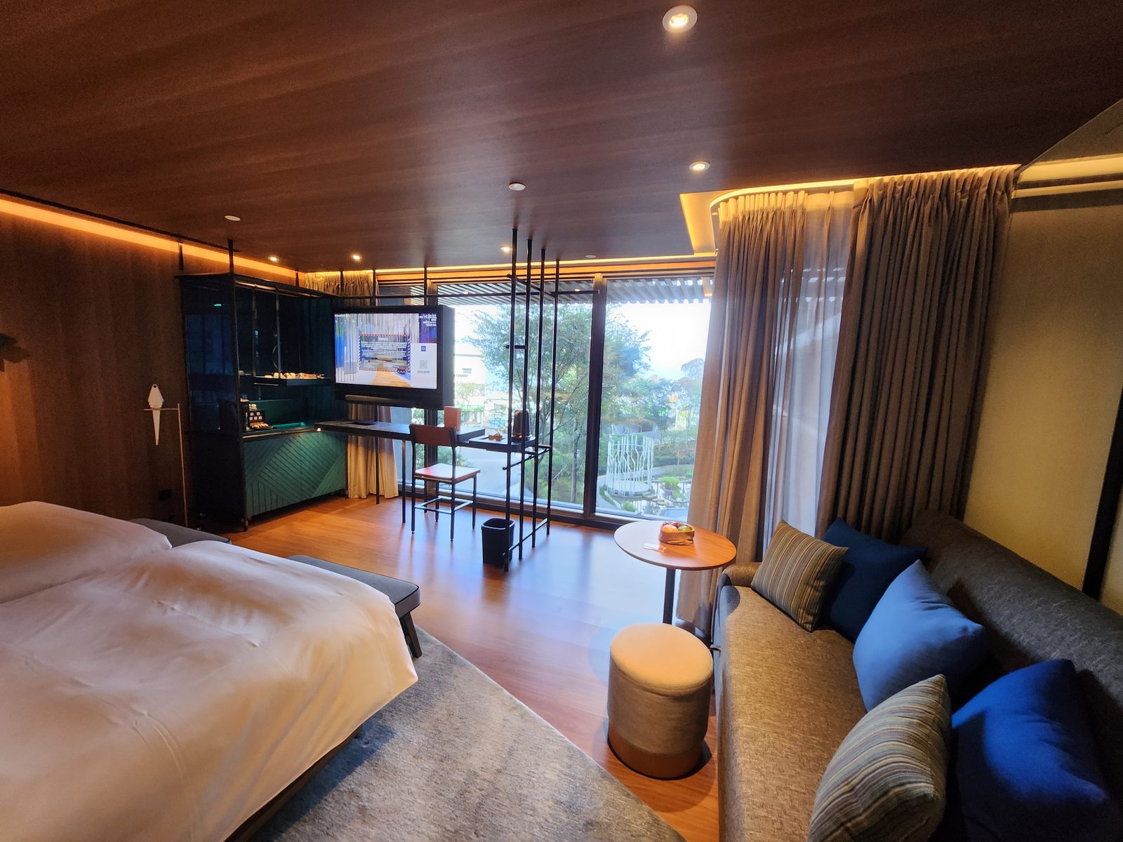 ภาพรวมห้องพักของโรงแรม Hotel Indigo Alishan เห็นเตียงใหญ่ มุมโซฟาริมหน้าต่าง และมินิบาร์สีเขียว