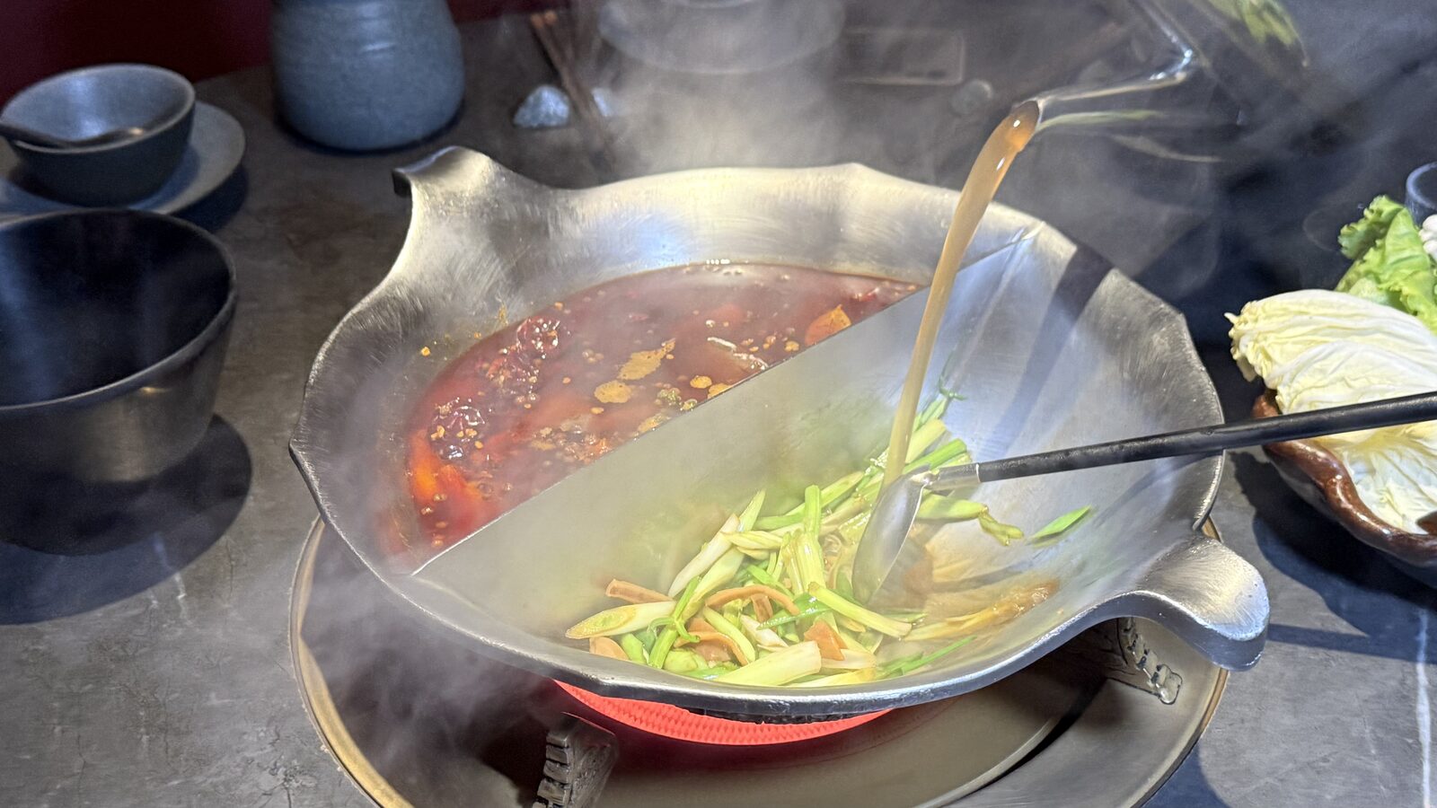 마늘대를 볶고 있는 냄비 한쪽에 직원이 주전자로 육수를 붓자 김이 피어오르는 모습