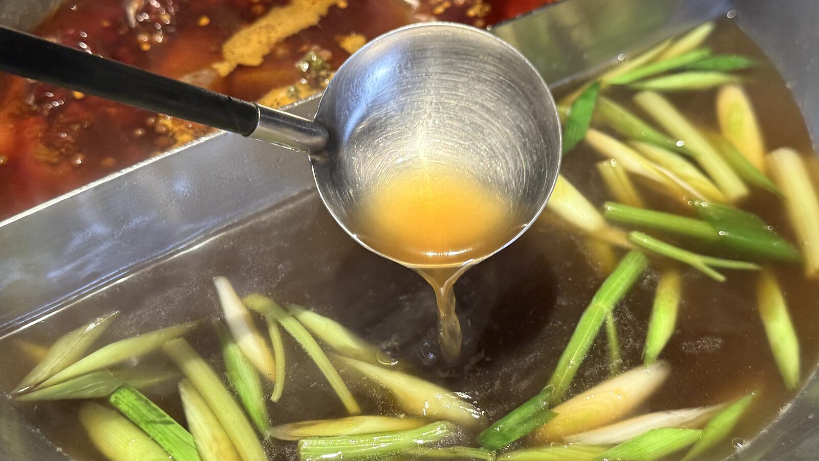 마늘대가 떠 있는 금빛 마늘 훠궈 육수를 국자로 떠 올린 모습