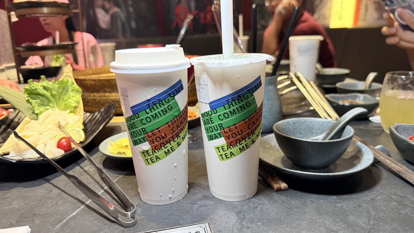 초록·파랑·주황 줄무늬와 GOOD THINGS ARE COMING YOUR WAY 문구가 인쇄된 음료 두 잔이 놓인 훠궈 테이블
