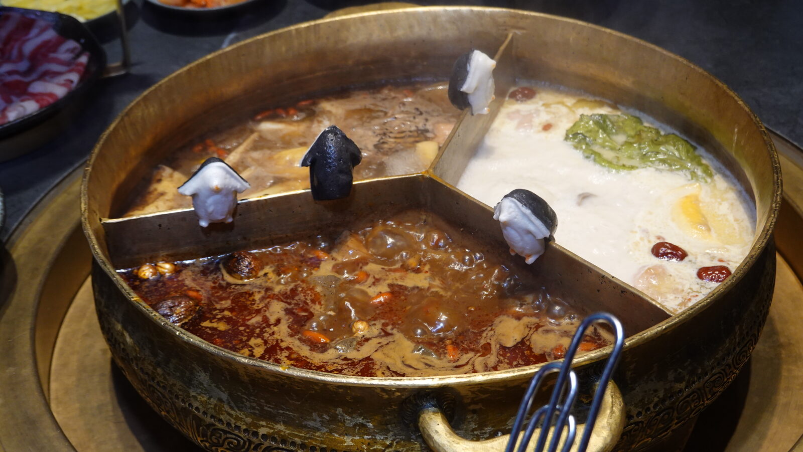 끓어오르는 3구 황동 냄비 클로즈업, 거품이 이는 마라 칸과 칸막이에 걸린 흑백 펭귄 모양 완자
