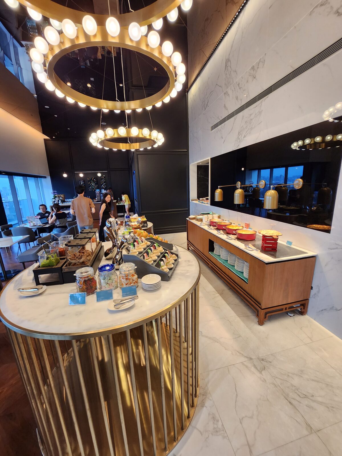 行政酒廊自助餐檯全景:金色圓形隔柵檯、熱食鍋與窗邊座席