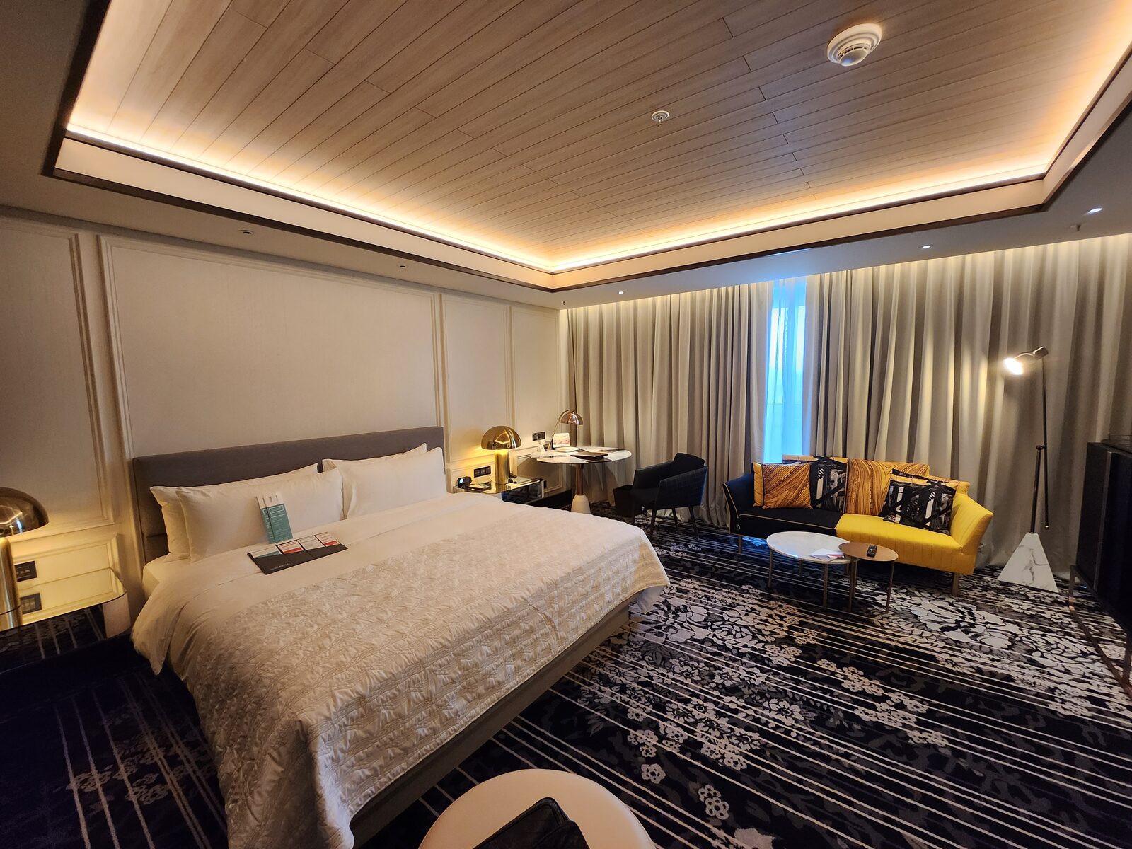 台中李方艾美酒店客房全景:大床、黑黃沙發、圓工作桌與黑白花紋地毯