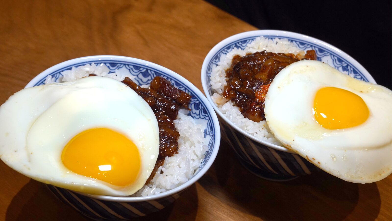 開囍滷肉專賣店雙碗招牌:經典原味黑金滷肉飯與獨門麻辣滷肉飯,覆蓋煎至微焦金黃的半熟荷包蛋