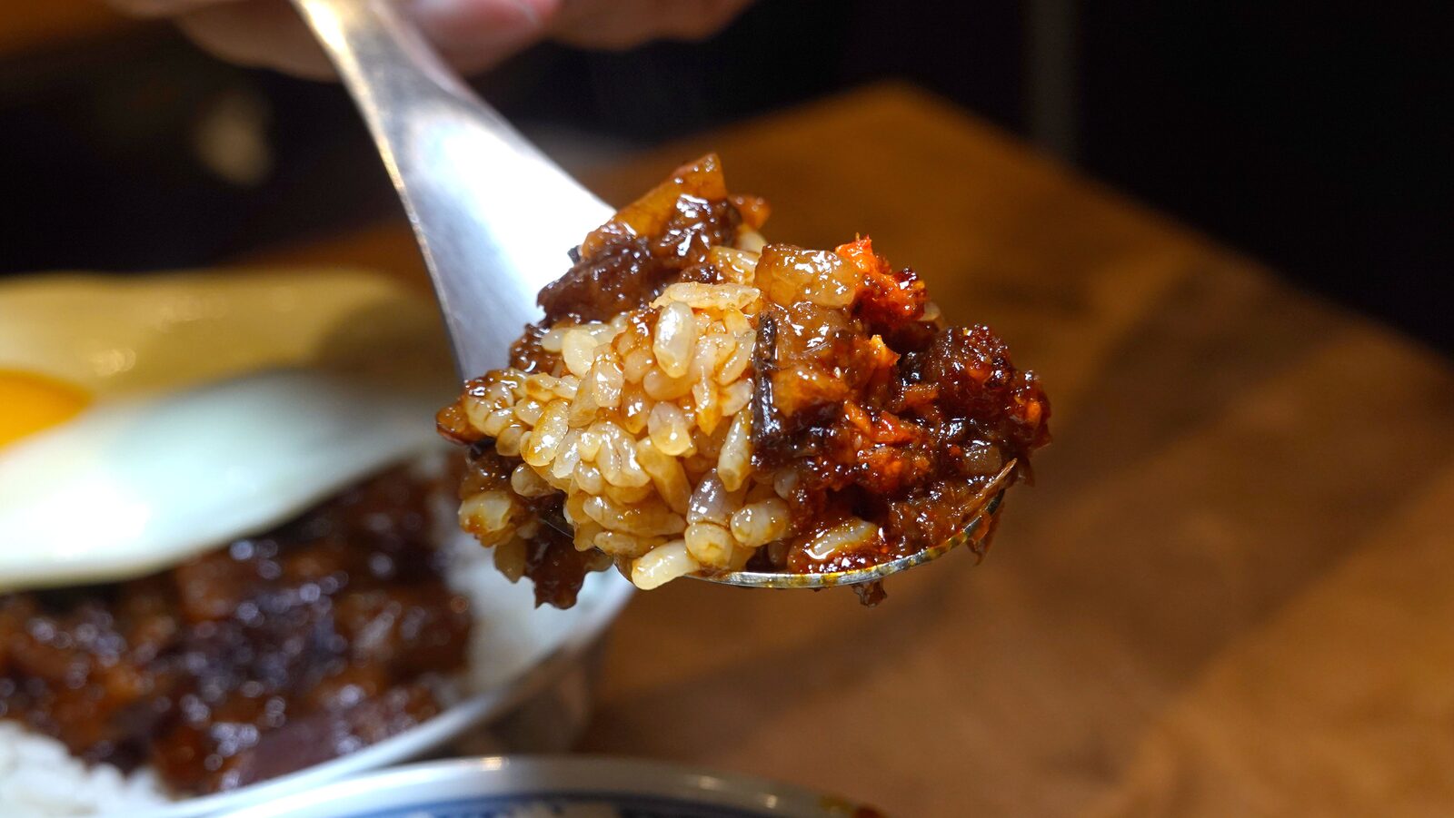 湯匙舀起一匙特製麻辣滷肉飯，帶有紅亮辣油與晶亮肉丁