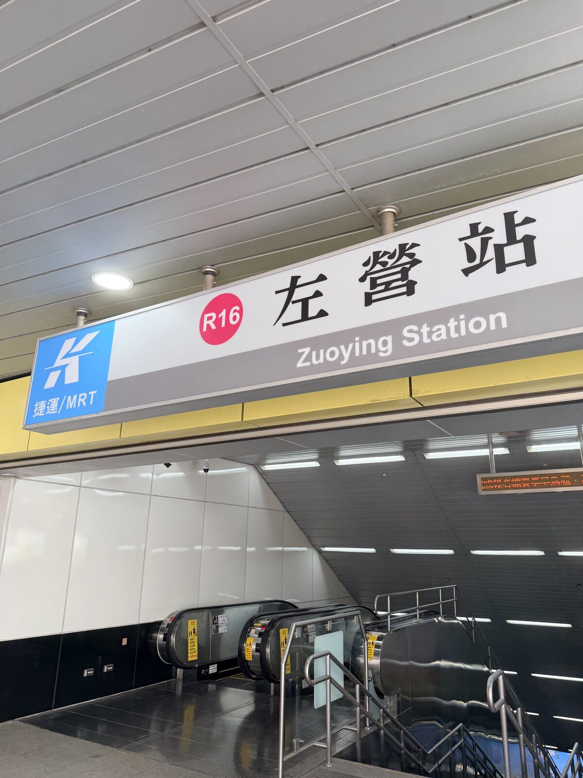高雄捷運R16左營站站名牌，下方是往月台的電扶梯