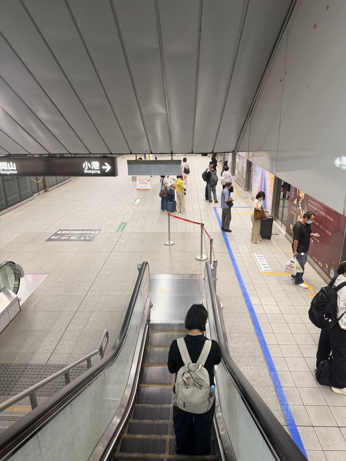高鐵左營站往下層的電扶梯，旅客背著背包沿指標前往捷運