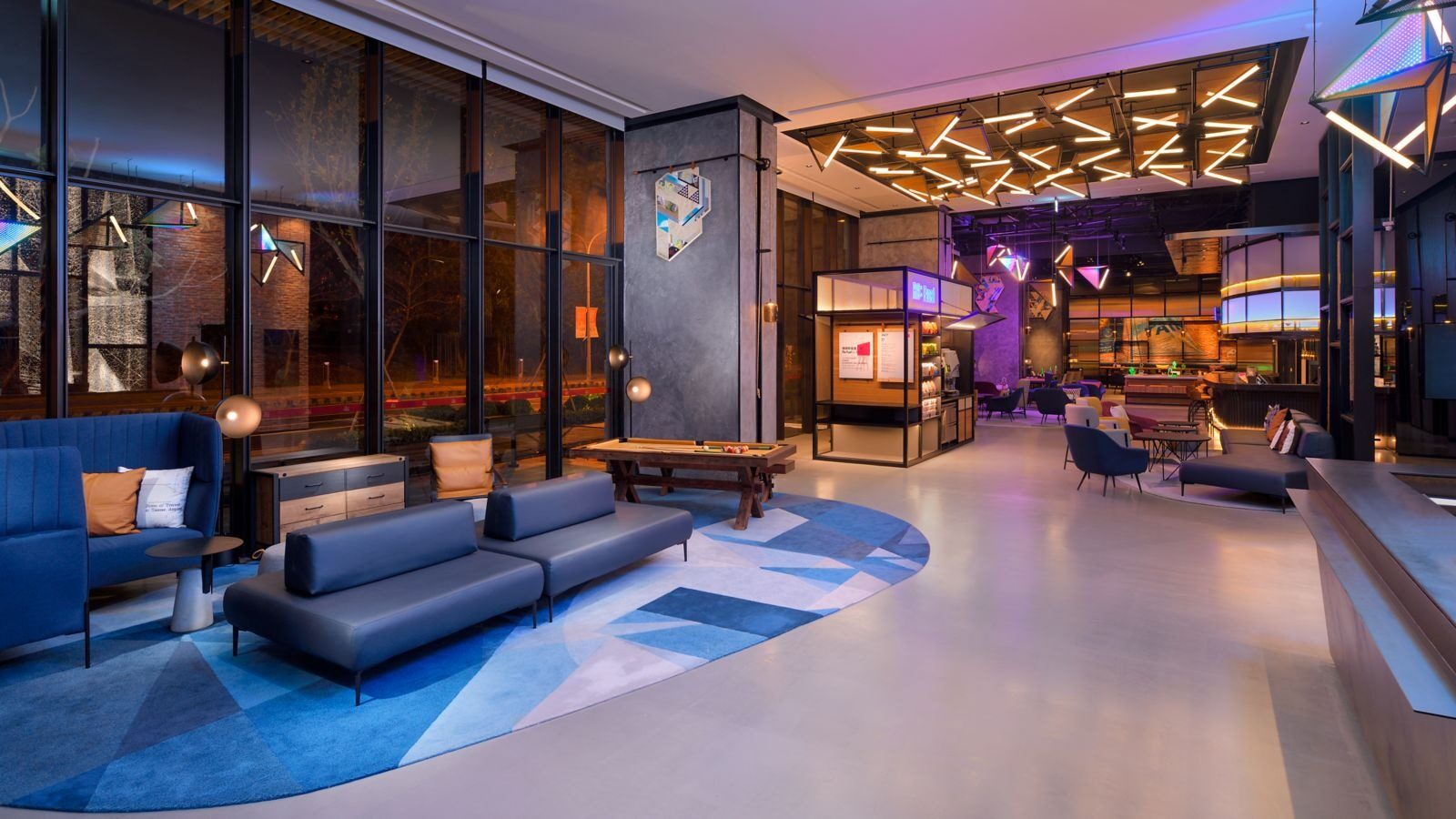 Blue sofas and a geometric-patterned carpet in the Re:mix Lounge in the lobby, with the night outside the glass windows