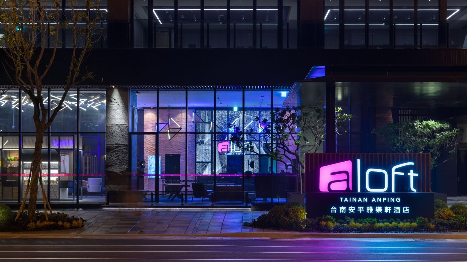 The hotel entrance at night, purple light glowing through the glass facade and an aloft sign out front
