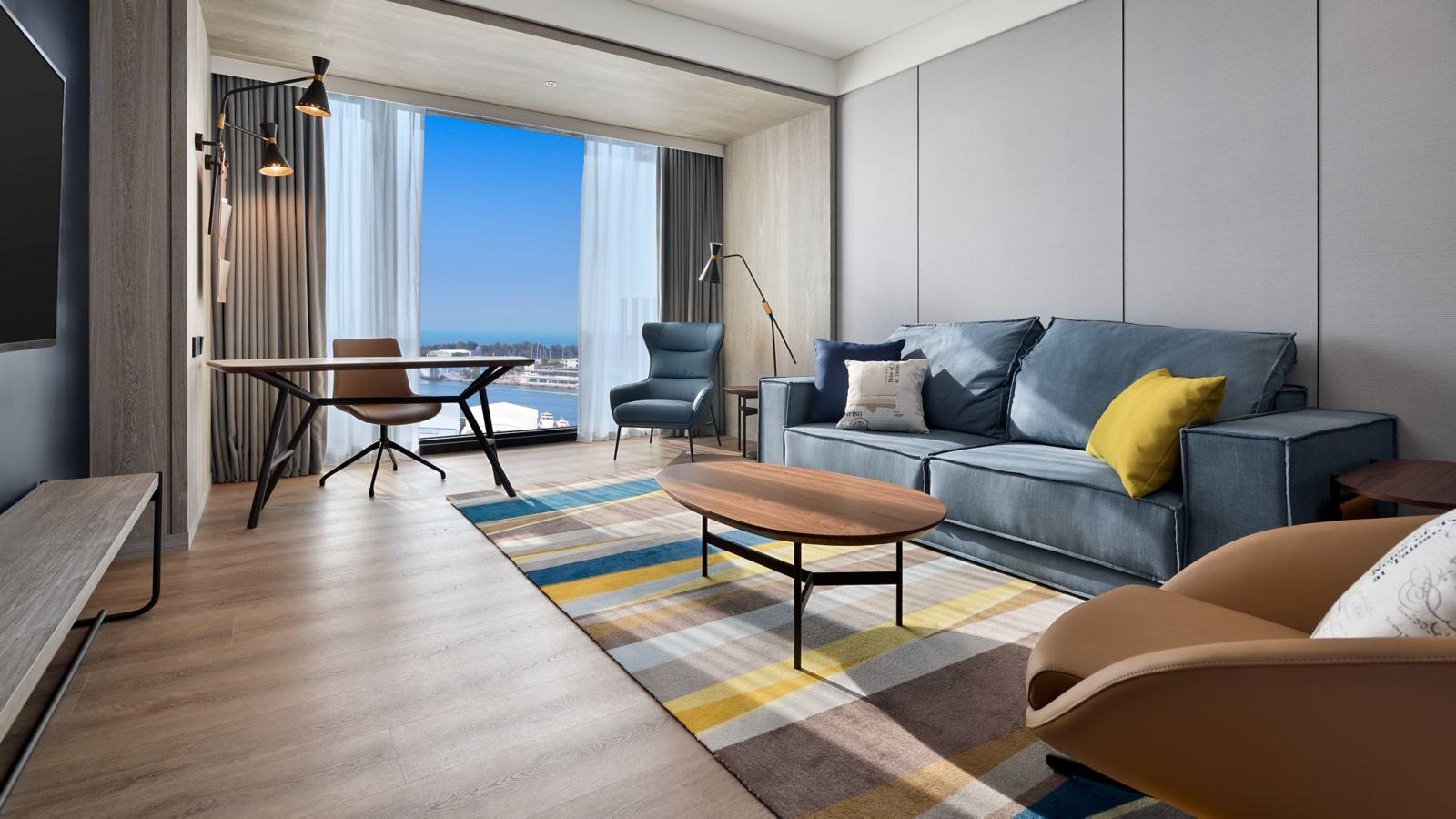 A blue-gray sofa and striped rug in a suite living room, with the harbor and water beyond the floor-to-ceiling windows