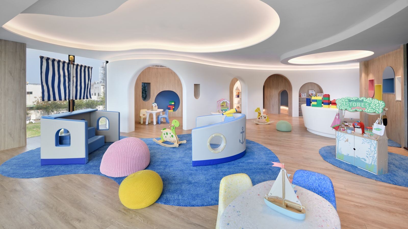 A kids' playroom with a blue carpet, colorful round cushions and an arch-shaped playhouse