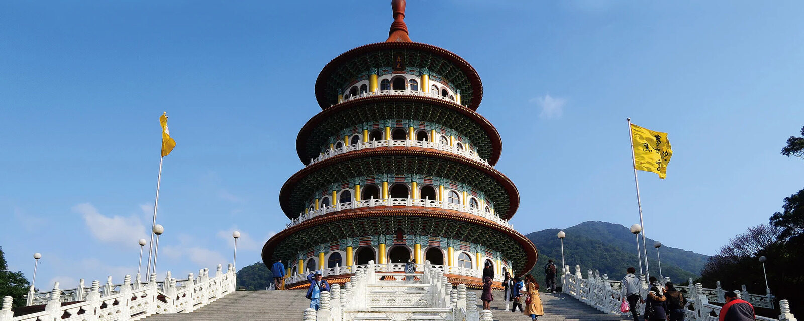 The tower of Wuji Tianyuan Temple under blue sky, with reddish-brown eaves on a green and yellow body, and visitors on the white-railed steps in front