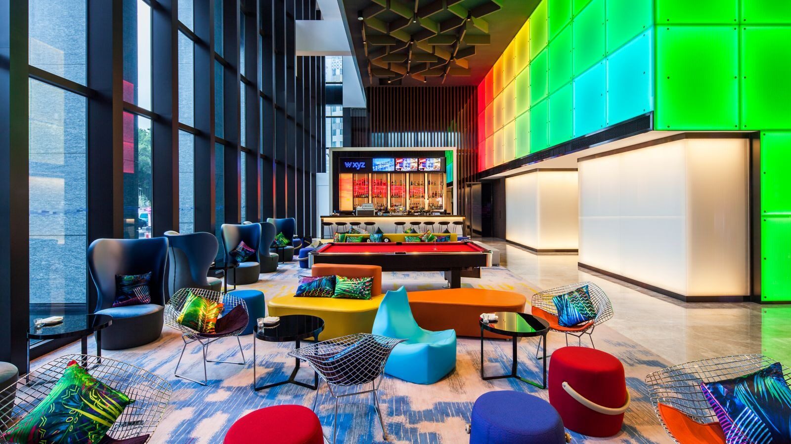 A pool table and colorful sofas beneath a multicolored light wall in the bar lounge