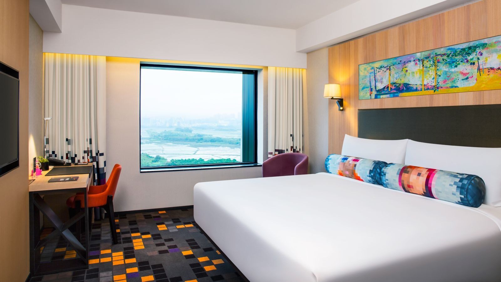 A river and plain beyond the large window of a king room, with a long, colorful painting above the headboard