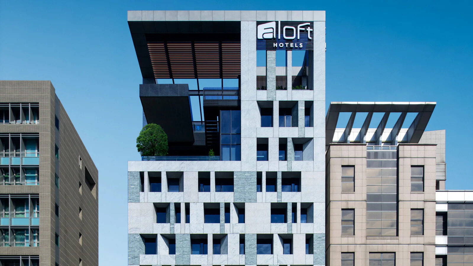 A building with a white grid facade under blue sky, an aloft sign on the roof