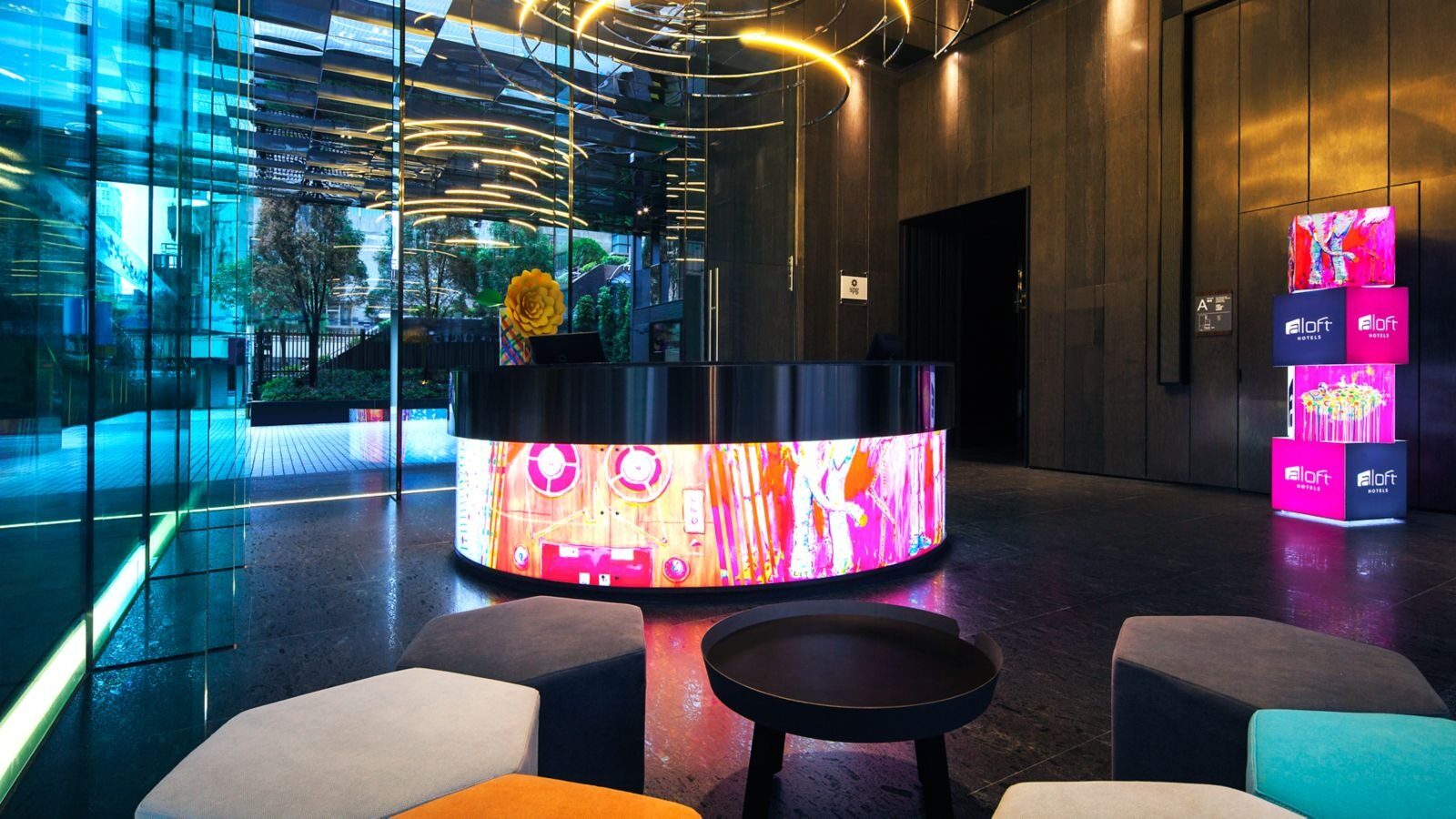 A glowing, multicolored curved reception desk in the lobby, beside aloft neon cubes and low seating