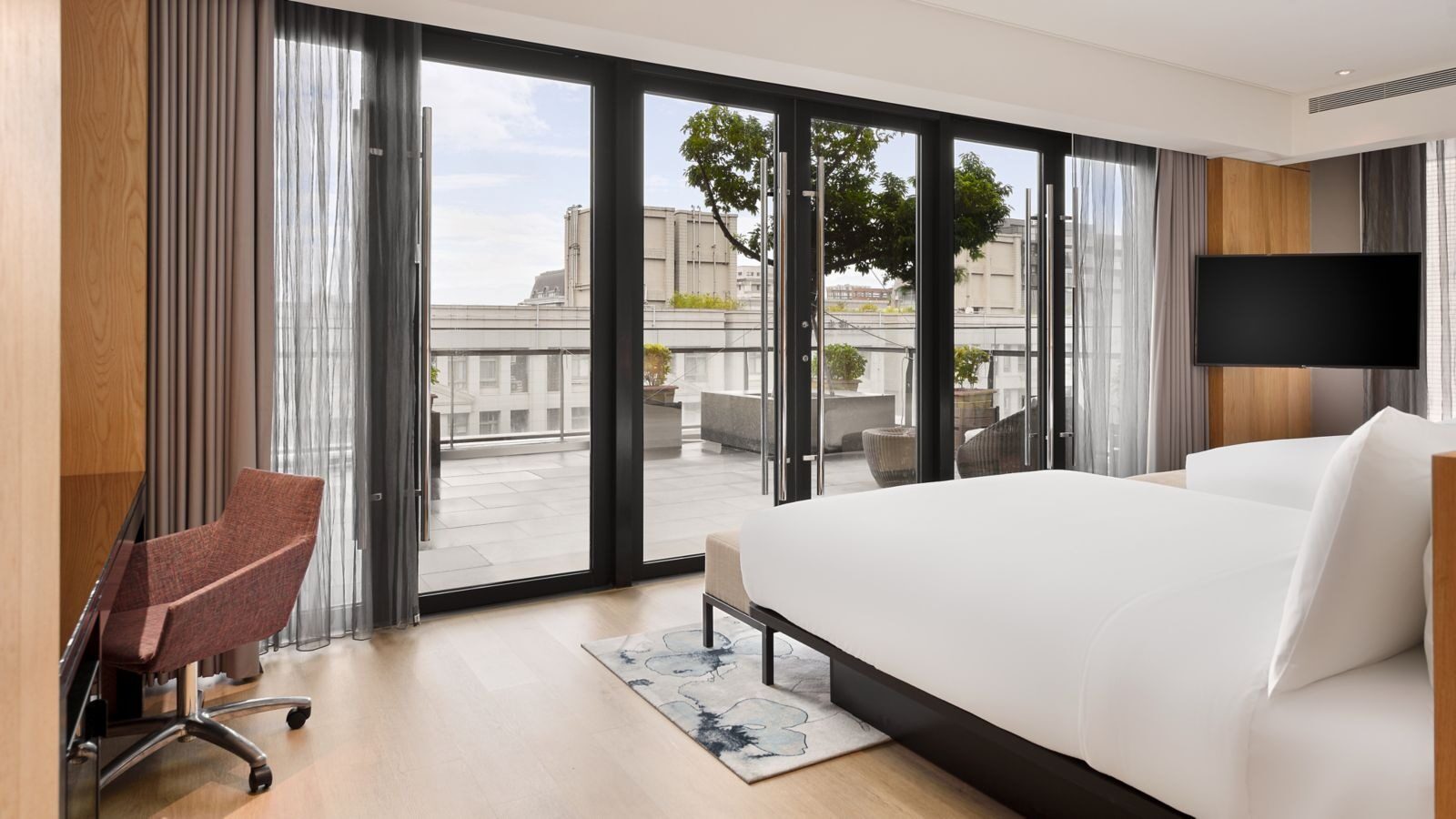 A wall of floor-to-ceiling glass doors beside the bed, opening onto a balcony and green trees