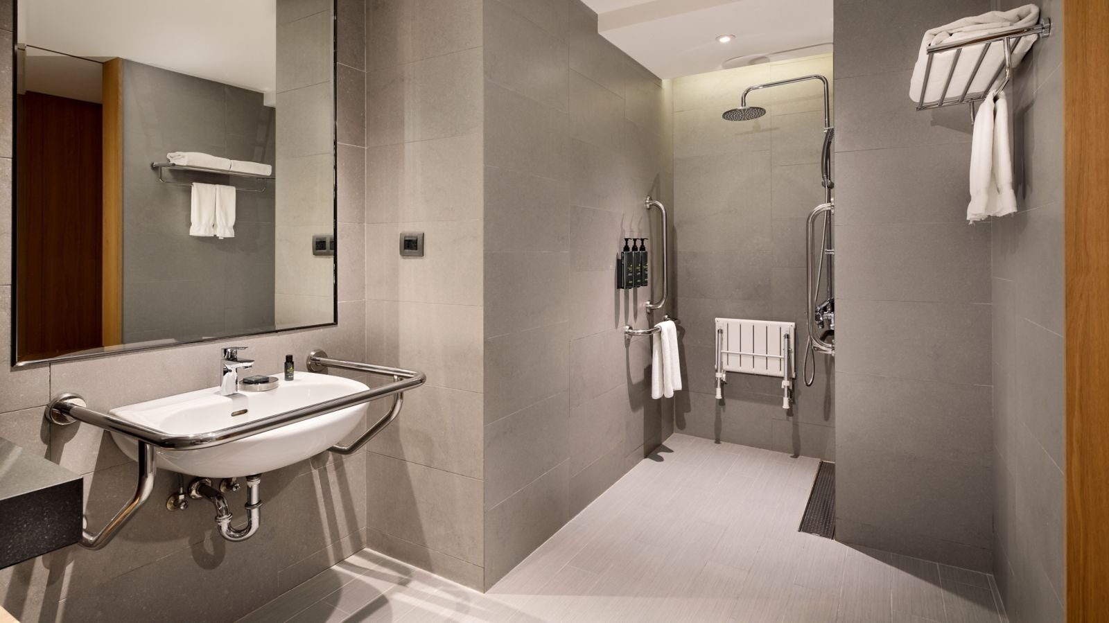 An open shower area in an accessible bathroom with grab bars, a folding shower seat and a handheld showerhead