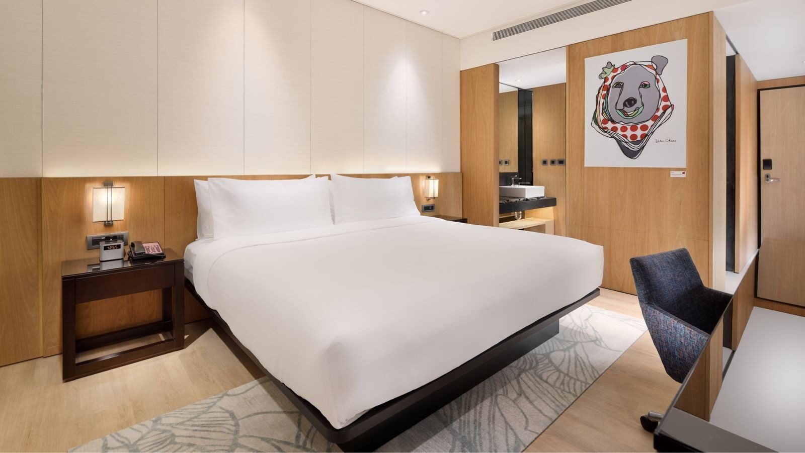 White bedding and a desk in a king room, with a bear illustration on the wall