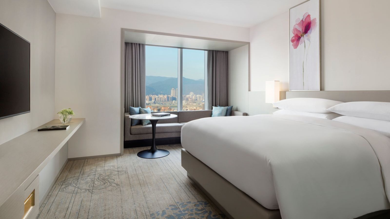 White bedding in a king room, with a small round table and chairs by the window and views of the city and mountains
