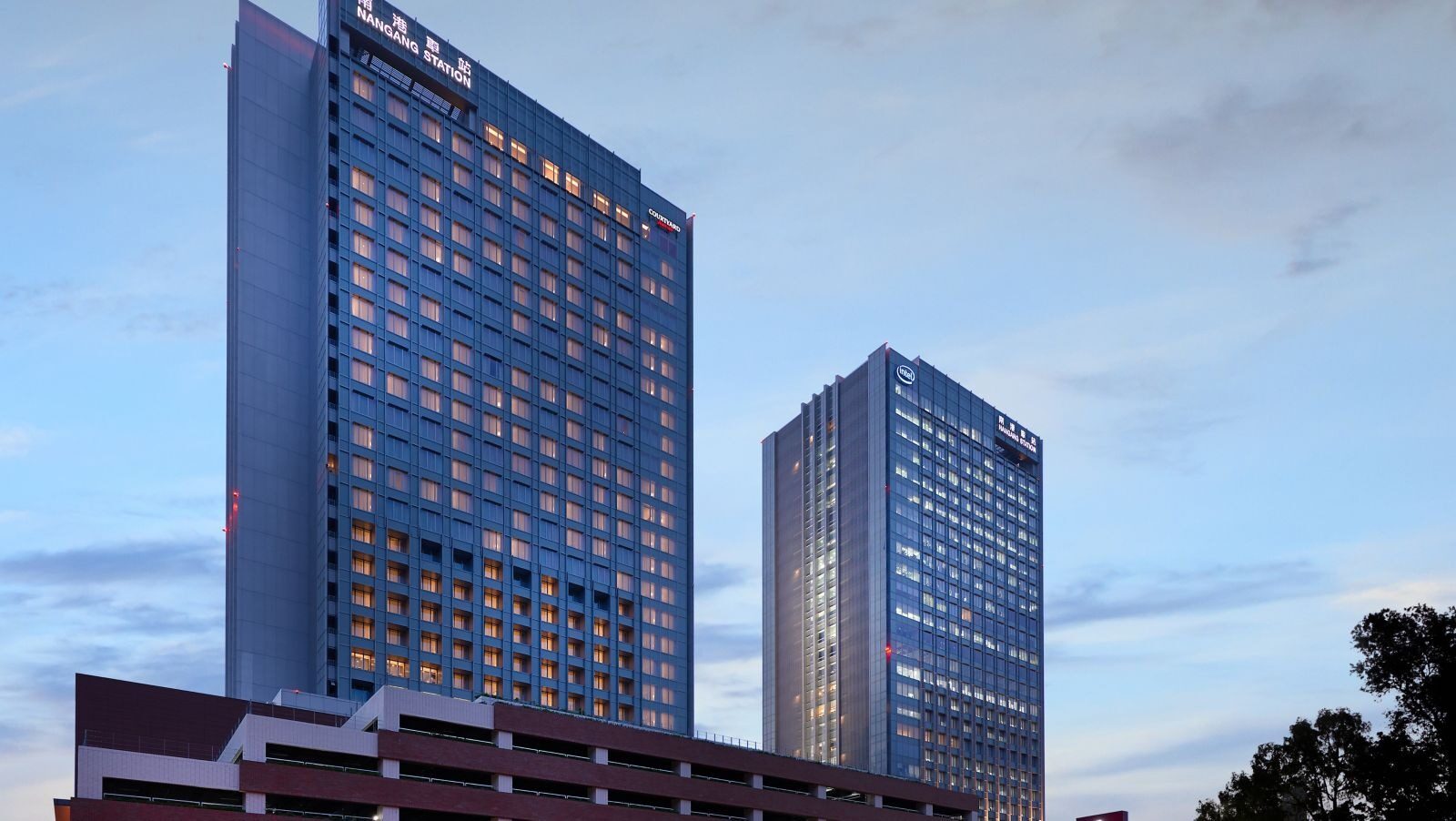 Two dark blue glass towers under blue sky, with a lower station building in front