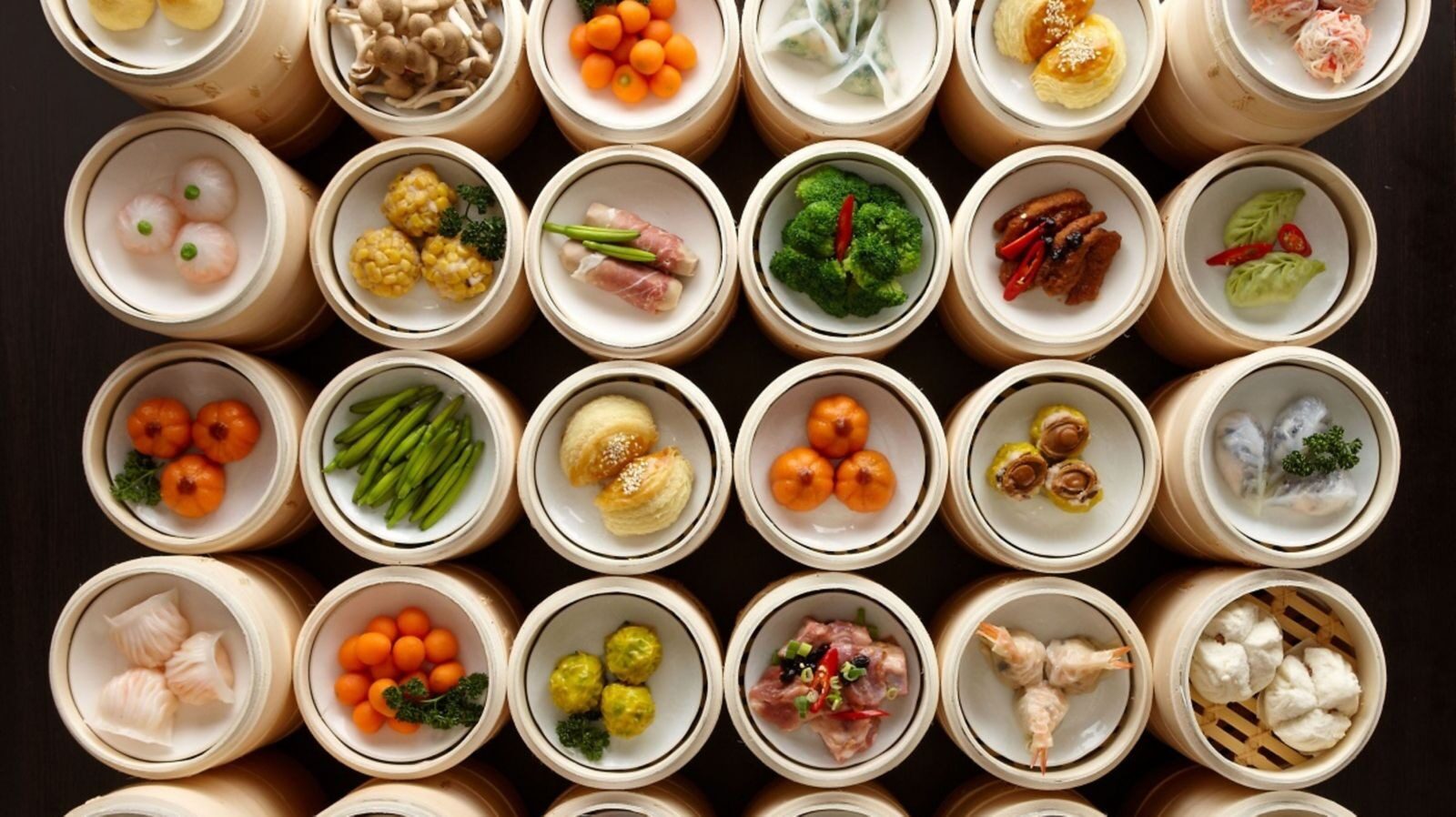 An overhead view of bamboo steamers and small white plates of har gow, siu mai and assorted Cantonese dim sum