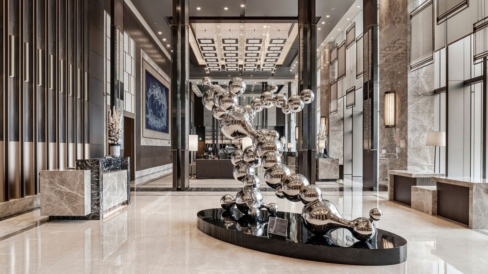 A human-shaped sculpture of strung silver spheres in the center of the high-ceilinged lobby, on pale marble flooring