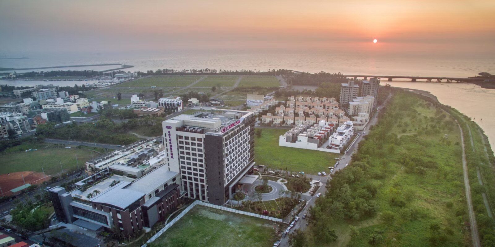 傍晚空拍安平一帶，酒店旁是大片綠地，遠方夕陽落在海面上
