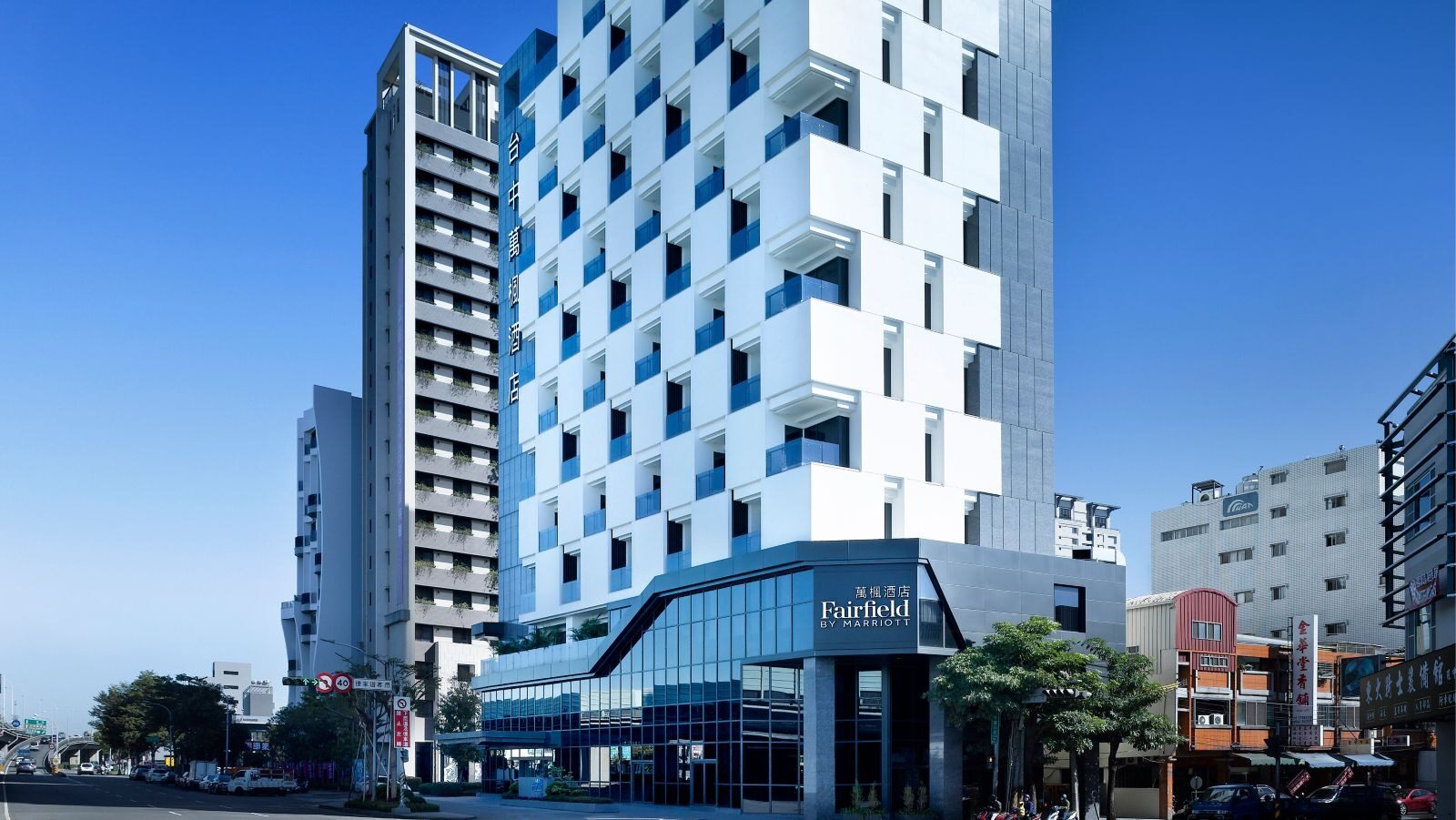 A white high-rise hotel under blue sky, its facade a staggered grid of windows above a glass-fronted entrance