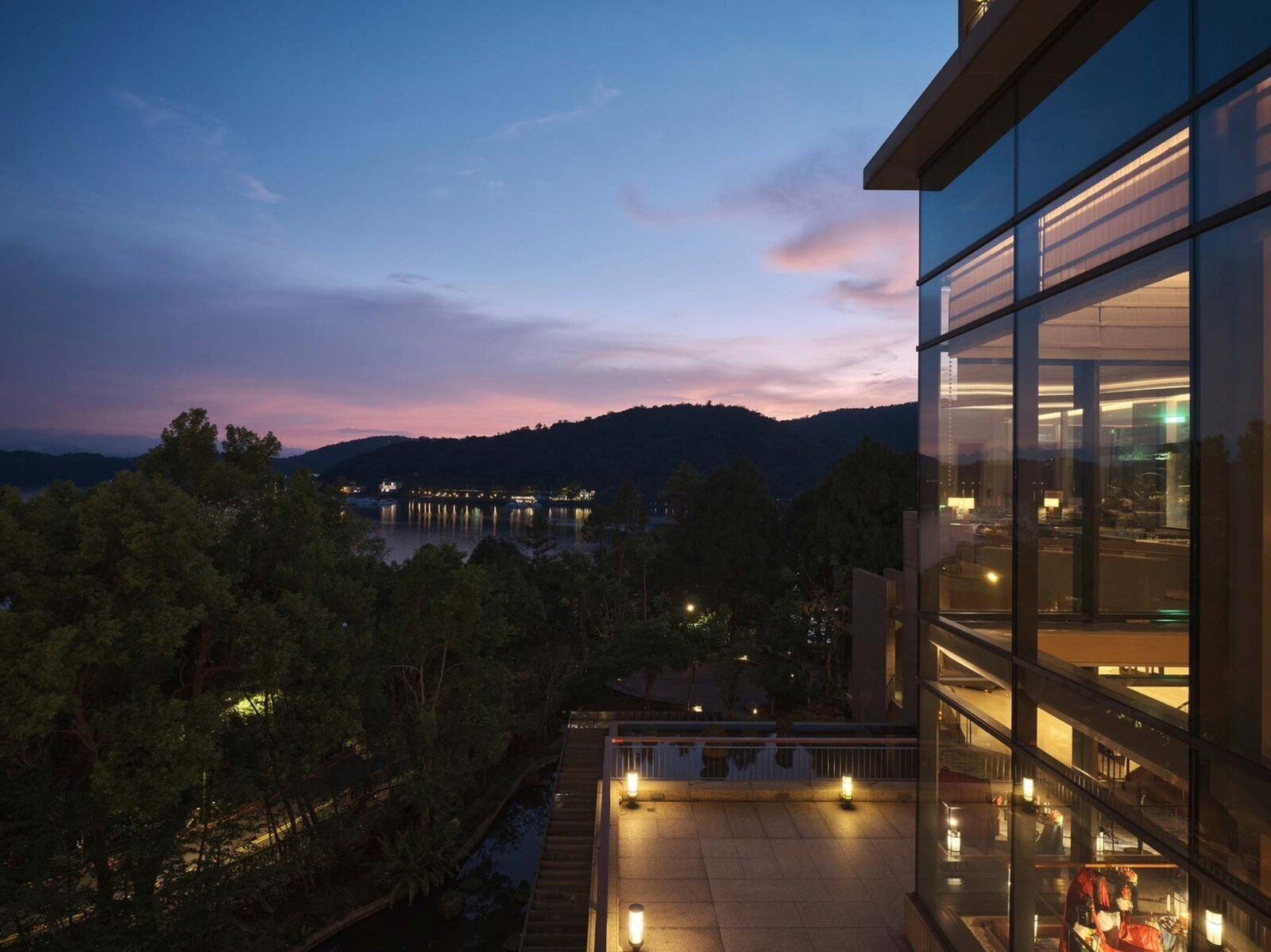 The hotel's lit glass facade and terrace at dusk, with ridgelines and sunset glow in the distance