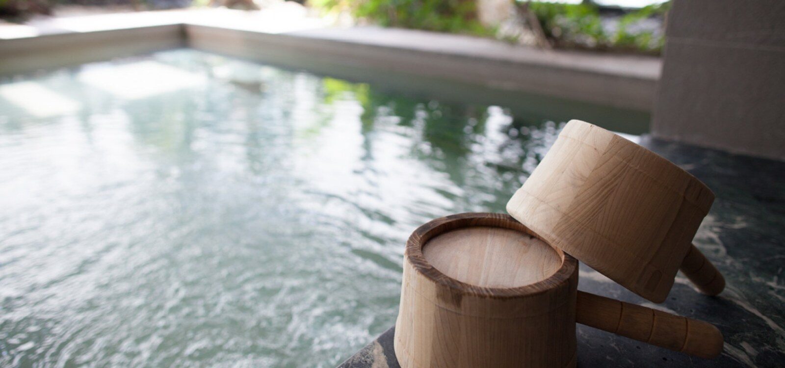 The surface of a hot spring pool with a wooden bucket and ladle at the edge