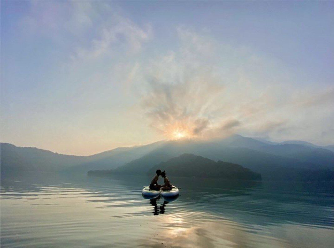 Silhouettes of stand-up paddleboarders on the lake at dawn with mountains behind