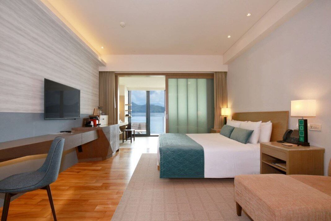 A lake-view king room with wooden floors, a large bed and floor-to-ceiling windows onto the balcony