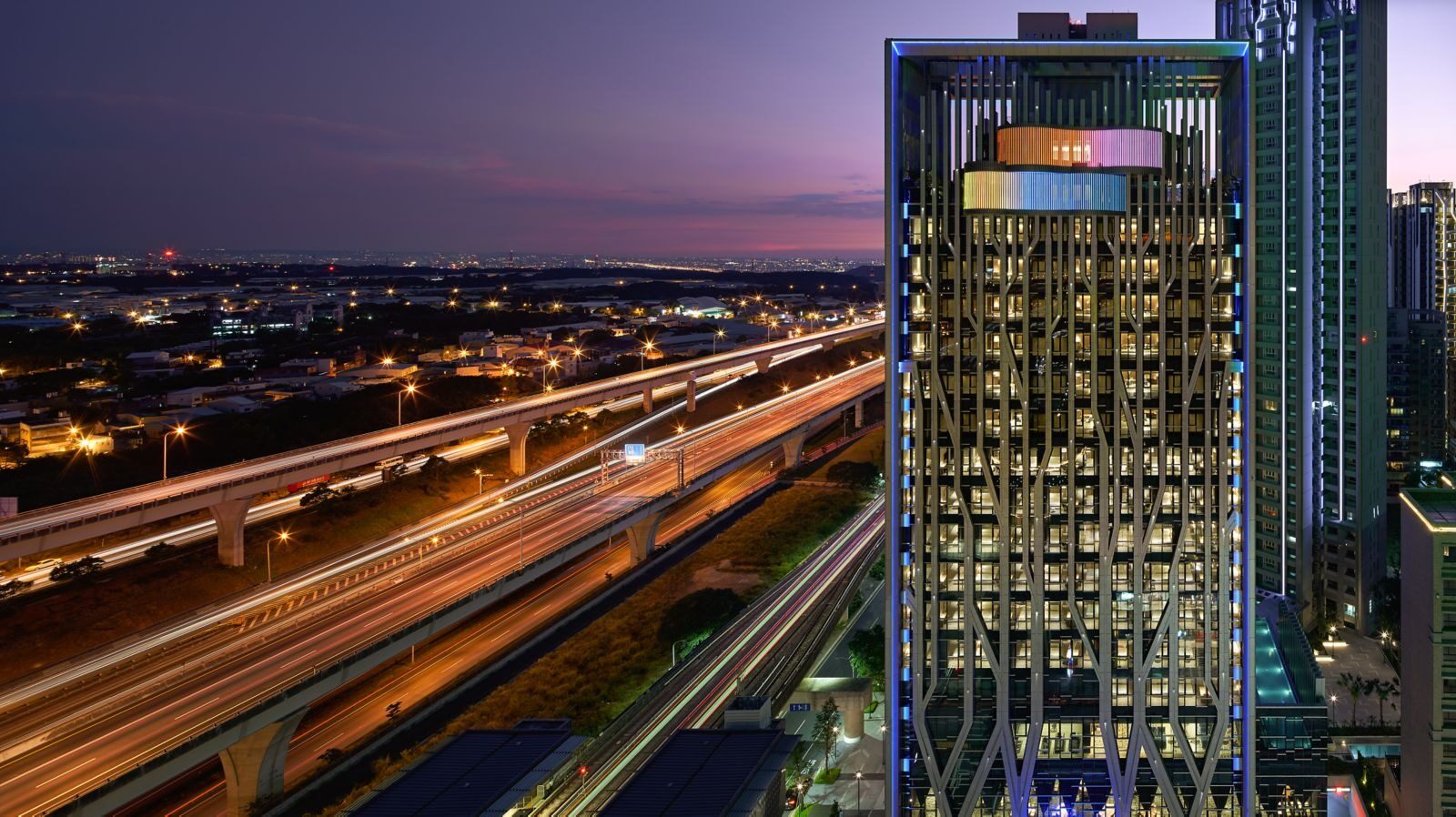 The hotel tower lit up at dusk, with light trails from traffic on the elevated road alongside