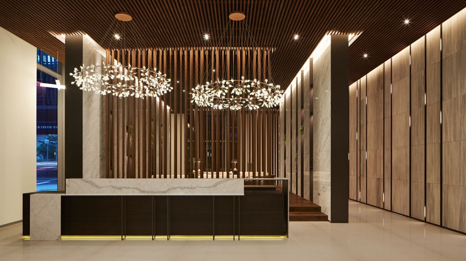 Branch-and-leaf chandeliers above the lobby reception desk, flanked by vertical wood-slat walls