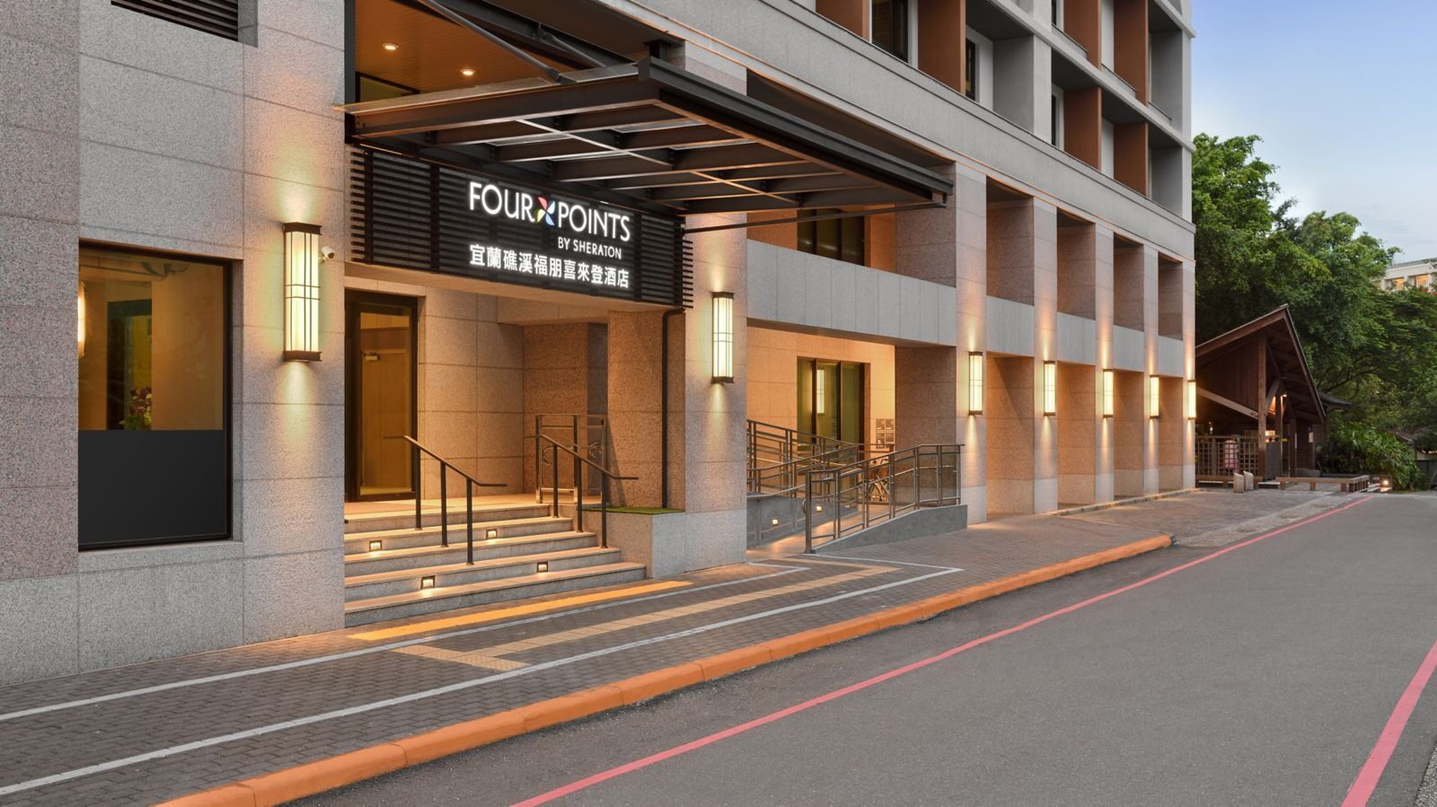 Steps, an accessible ramp and a Chinese and English name sign at the hotel entrance, a red-lined road in front and green trees and wooden eaves in the distance