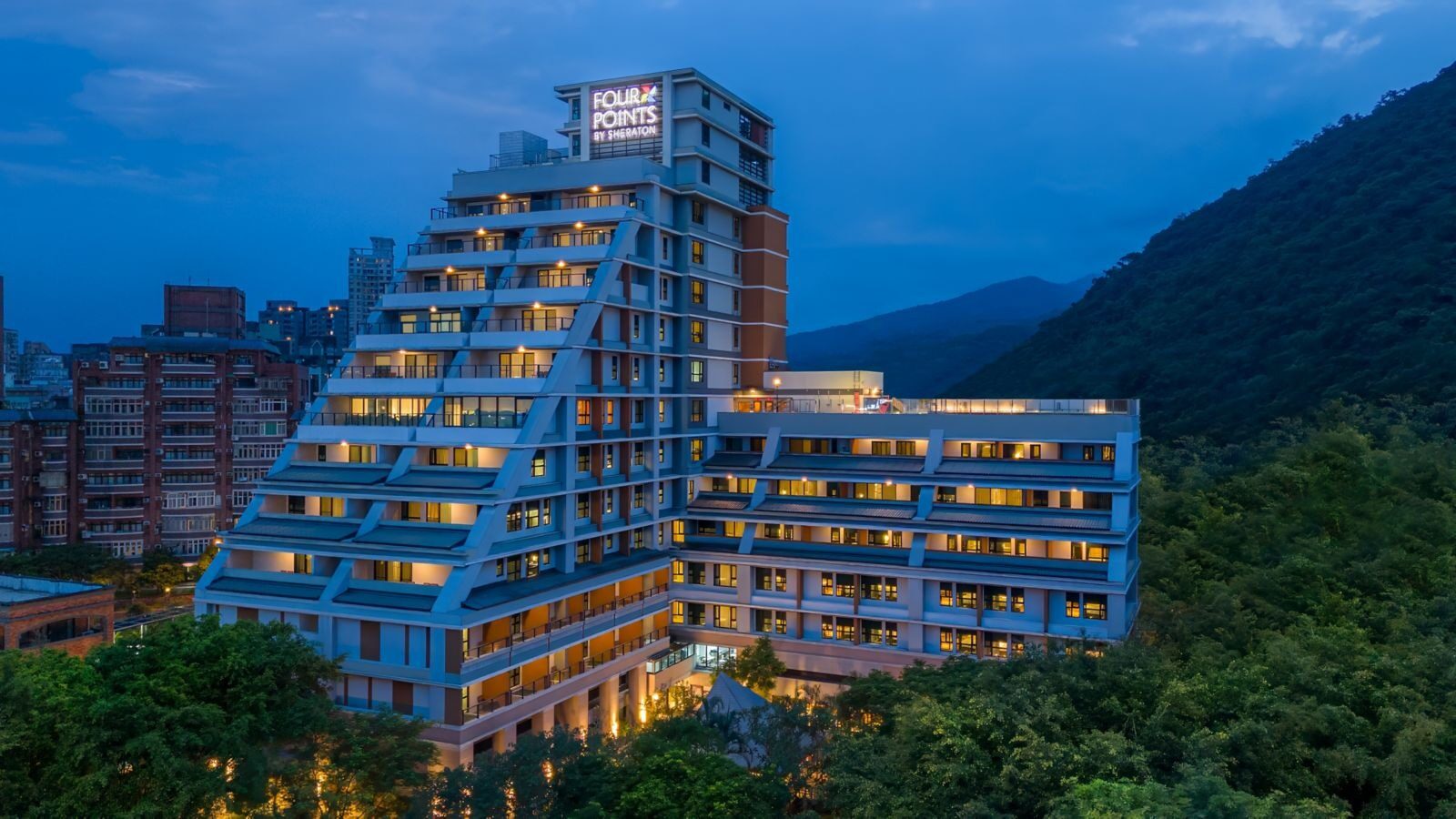 The terraced hotel building lit up at dusk, with green hillsides behind