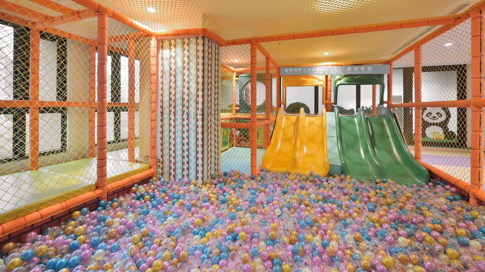 A colorful ball pit, slide and orange net climbing frame in the kids' play area
