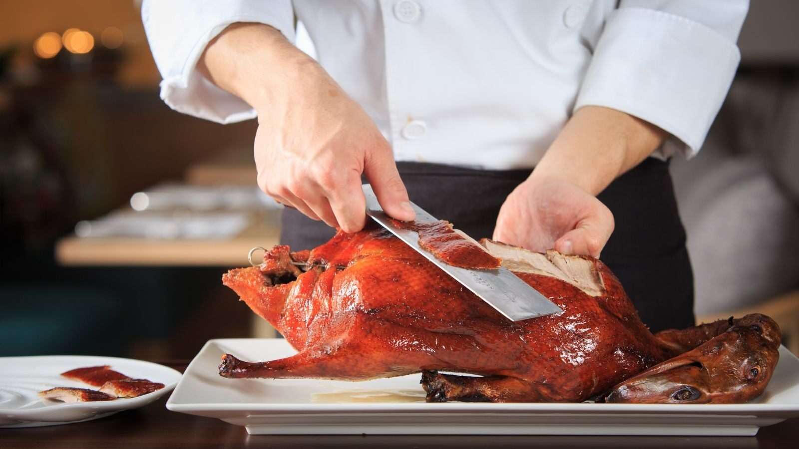 A chef carving a whole glistening roast duck at the counter