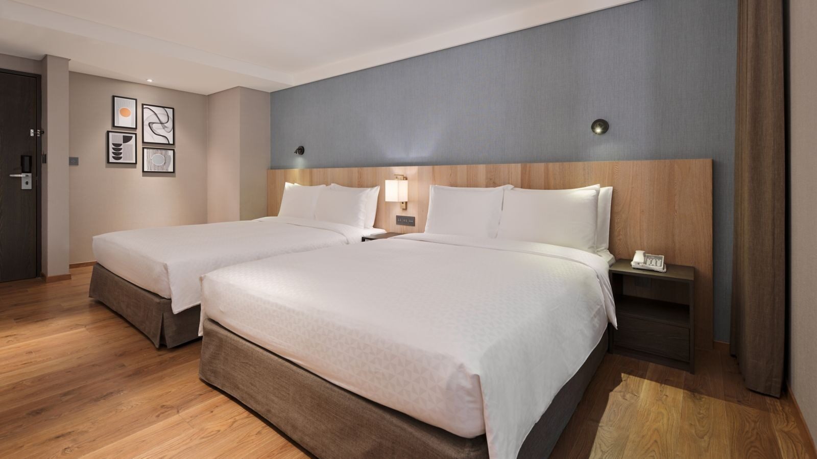 Two large beds side by side in a family room, with wood floors and pale blue-gray walls
