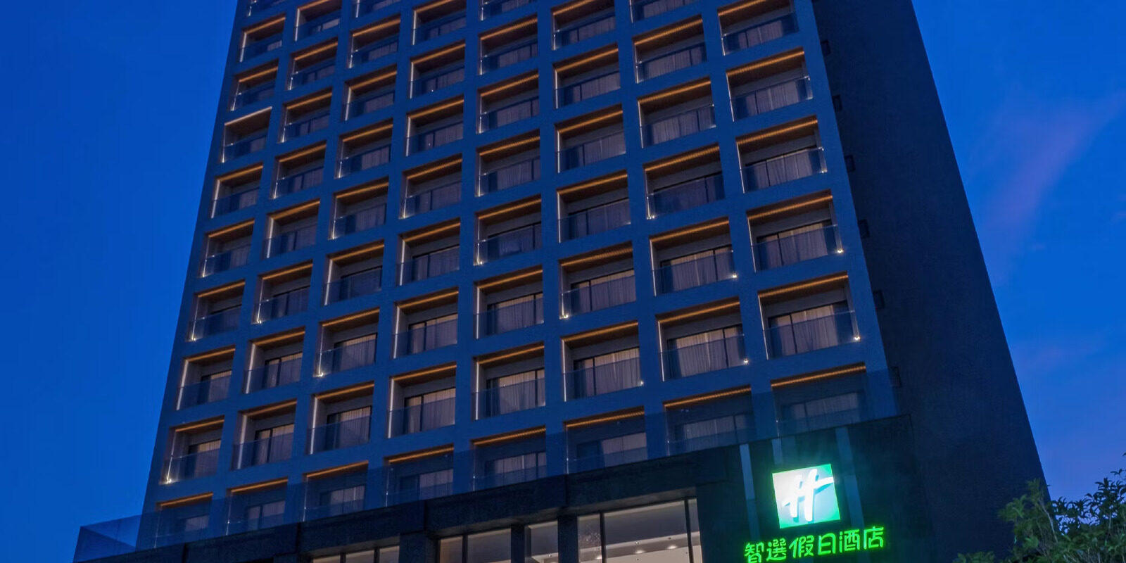 The dark blue tower of Holiday Inn Express Chiayi at dusk, with a green sign lit up on the lower floors