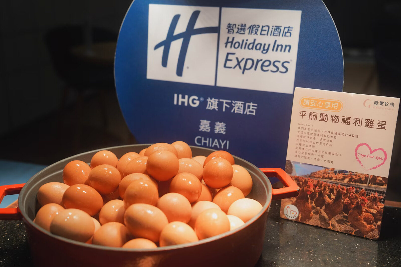 A red cast-iron pot piled with brown eggs, next to a Holiday Inn Express sign and a card explaining the cage-free eggs