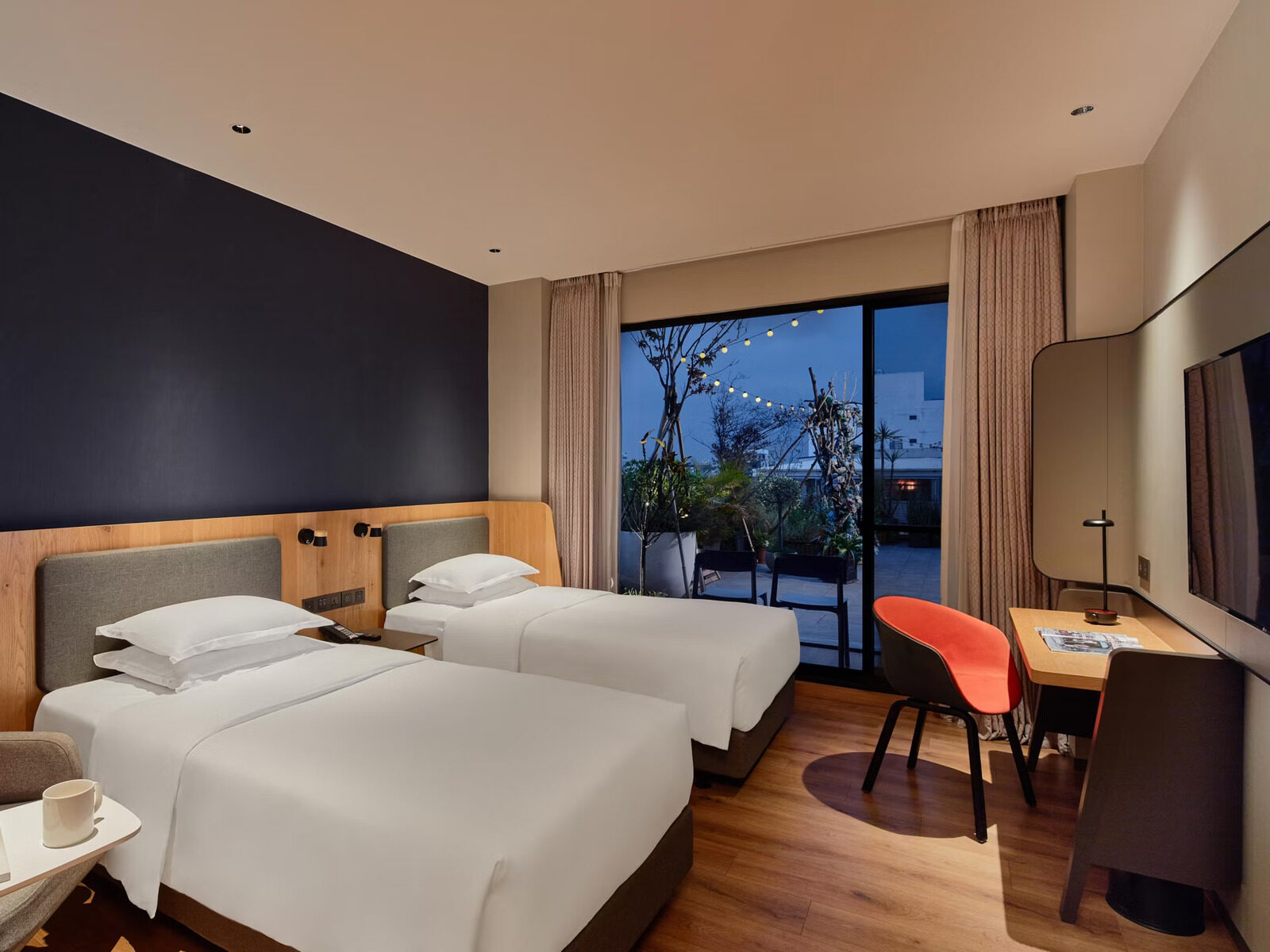 A twin room whose glass doors open onto a balcony strung with lights and set with potted plants