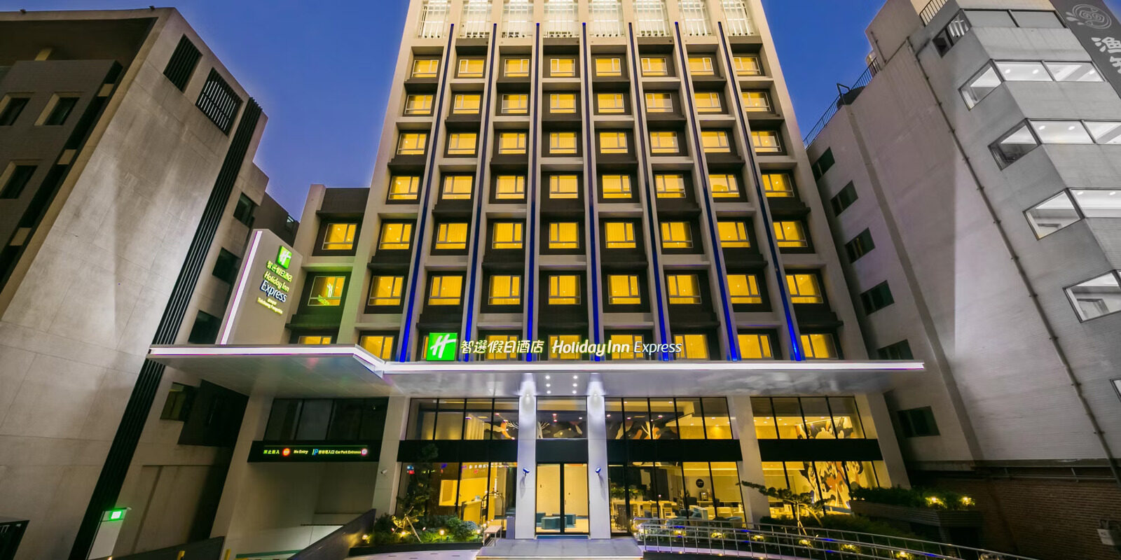 The lit-up facade of Holiday Inn Express Taichung Fengchia at night, with warm yellow light glowing from rows of windows