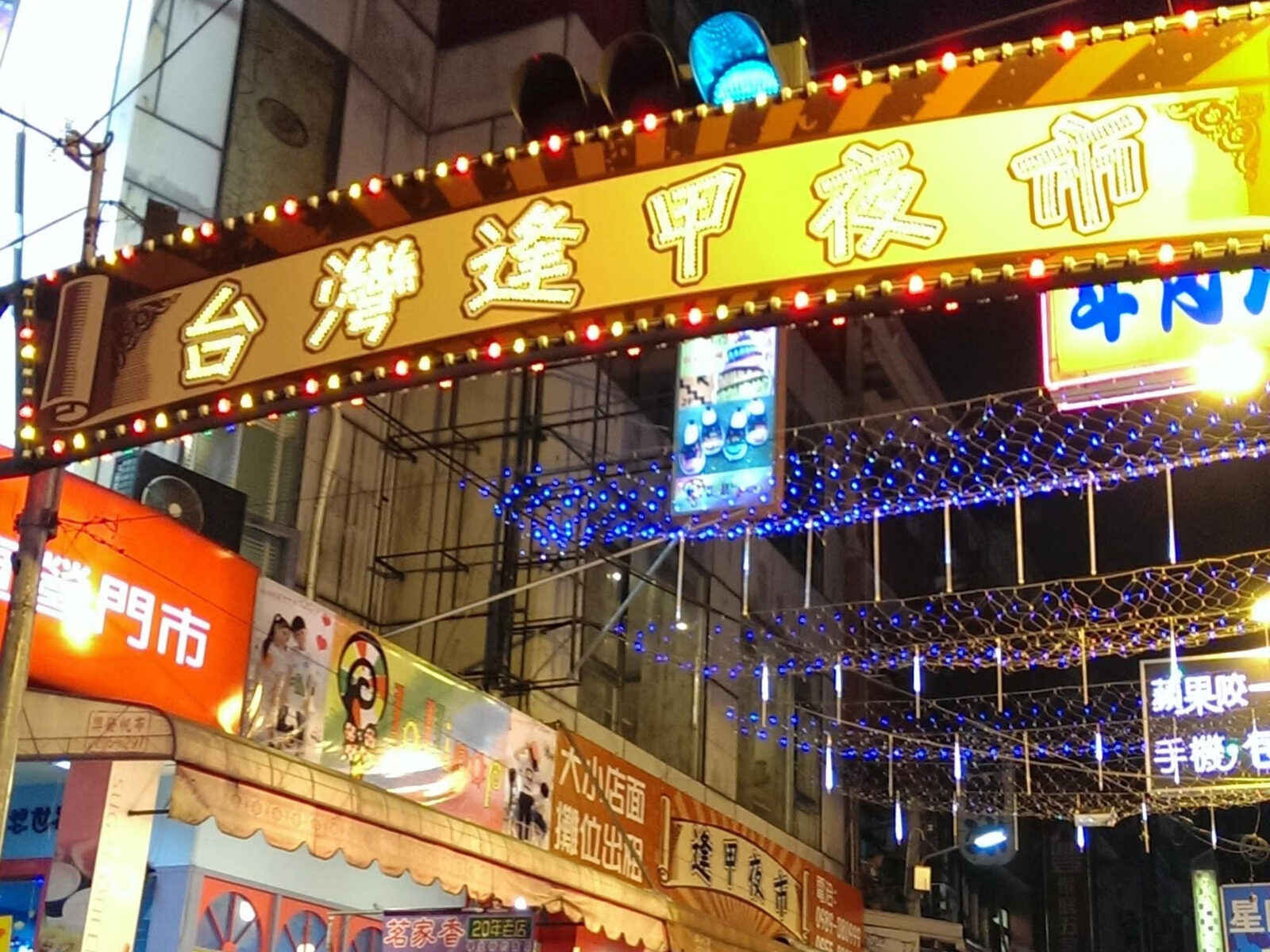 夜晚的逢甲夜市入口，霓虹招牌写着台湾逢甲夜市，上方挂满蓝色灯串