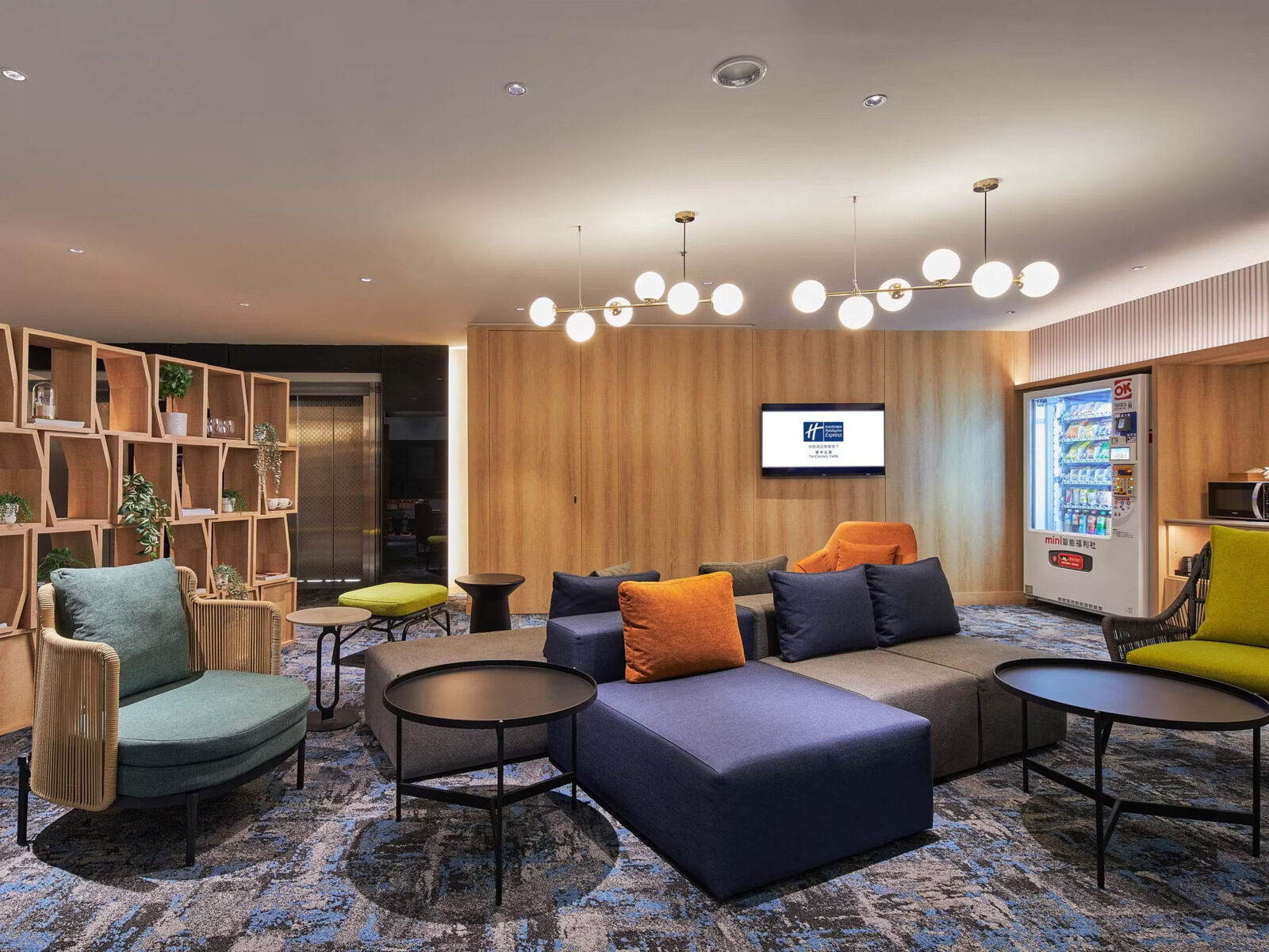 Dark blue sofas and round tables in the lobby lounge, with wooden bookshelves and vending machines behind