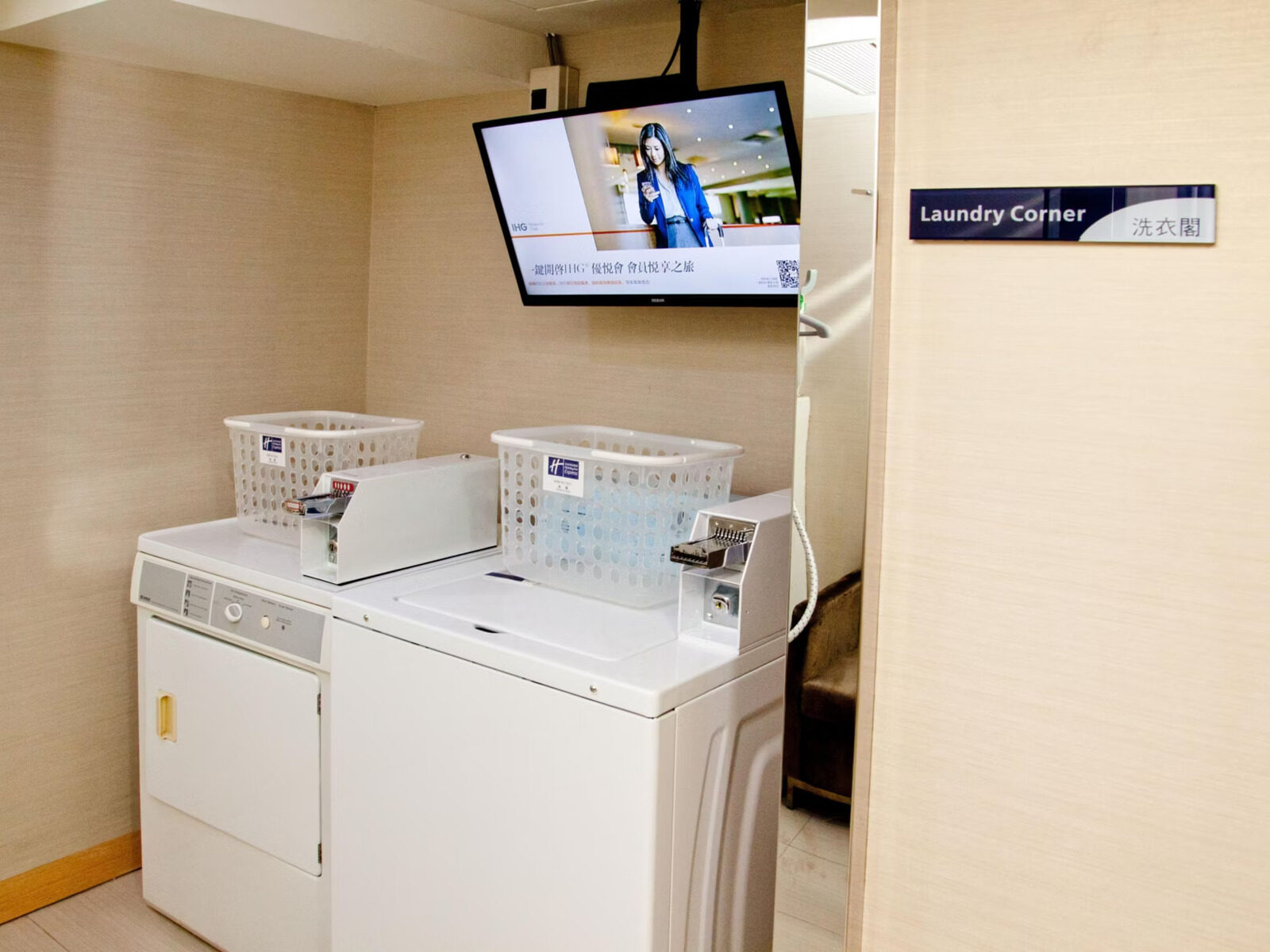 A white dryer and washing machine side by side with a TV mounted above, and a Laundry Corner sign on the wall to the right