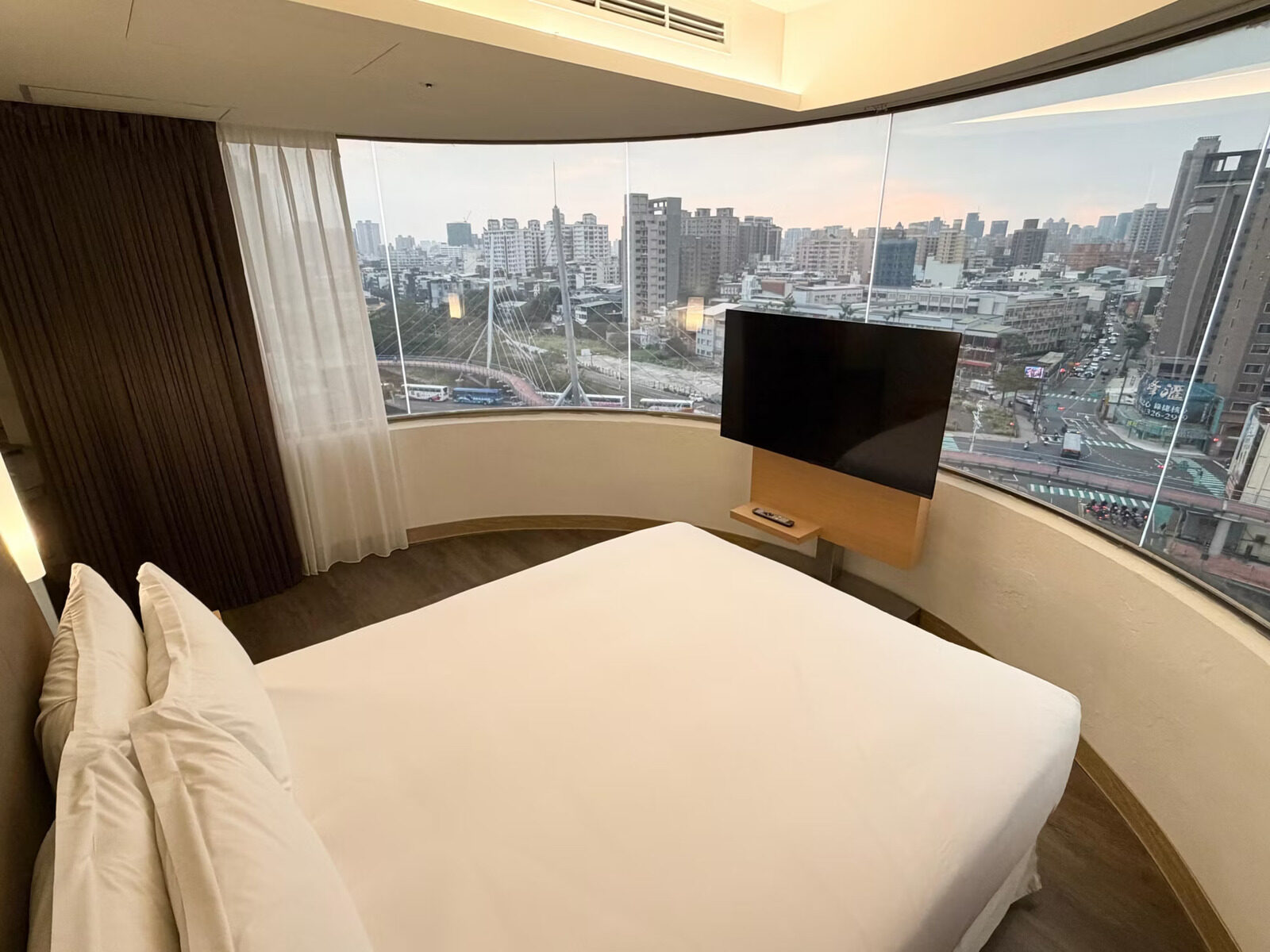 Central Taoyuan beyond curved floor-to-ceiling windows, with a car park full of coaches, an S-shaped skybridge and traffic at the intersection below