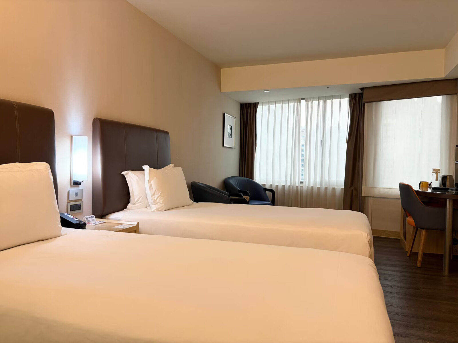 A room with two single beds side by side, a desk and an armchair by the window