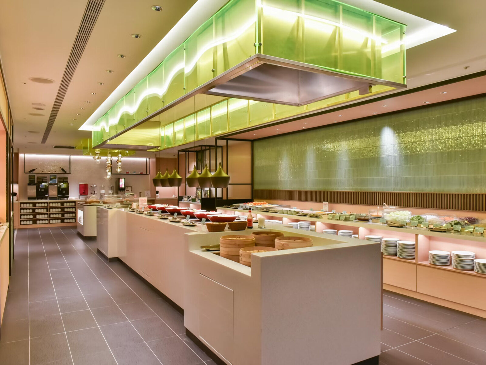 长条形自助餐台摆满菜肴与餐盘，上方是绿色灯箱